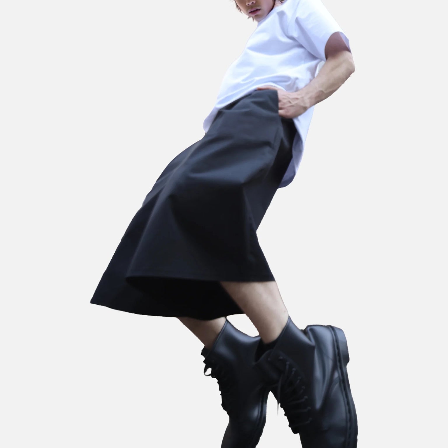 Homme en mouvement portant le bermuda Shaka noir, coupe ample inspirée du hakama japonais, associé à un t-shirt blanc et des boots noires
