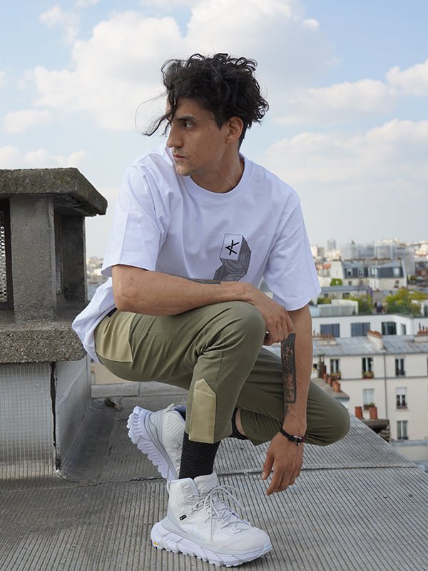 Homme accroupi en extérieur portant un pantalon Taitsu kaki, coupe droite ajustée à la cheville, avec empiècements contrastés et fermeture magnétique