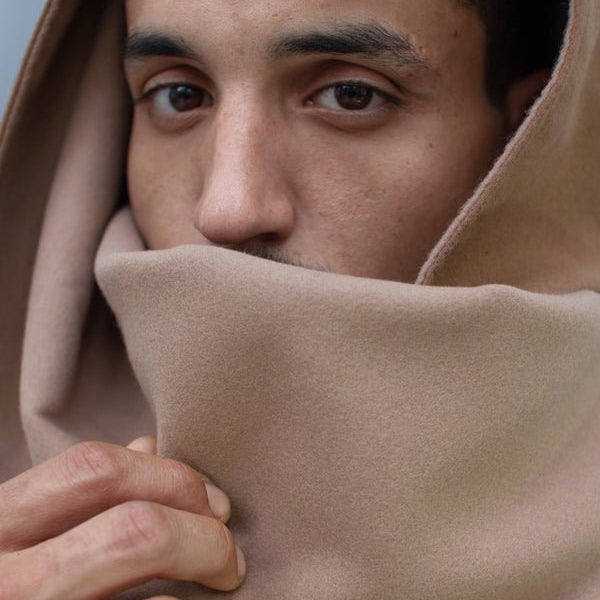 Portrait rapproché d’un homme portant une écharpe beige en polyester recyclé, portée en capuche et cache-cou, avec finition douce et fermeture invisible par aimants