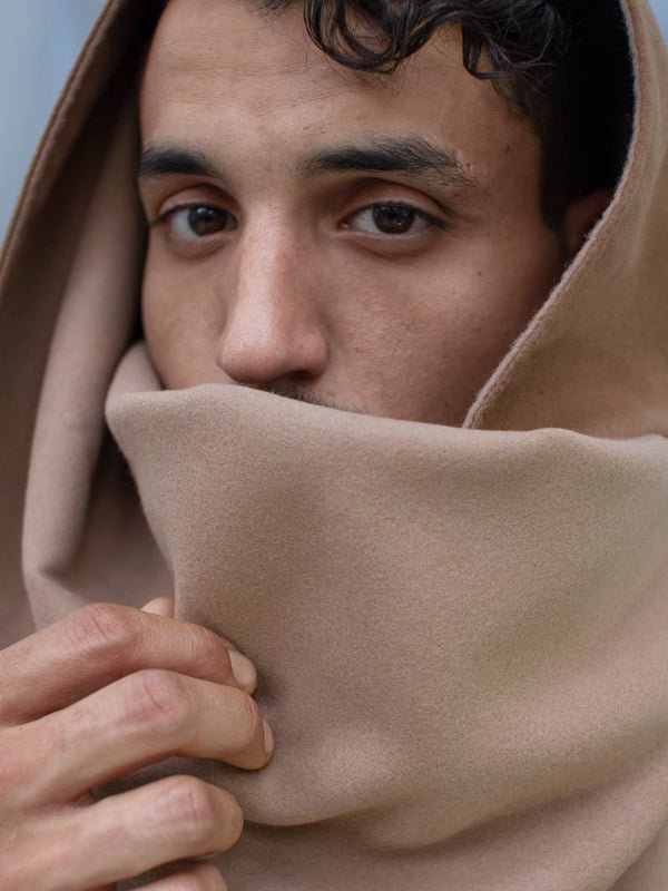 Portrait rapproché d’un homme portant une écharpe beige en polyester recyclé, portée en capuche et cache-cou, avec finition douce et fermeture invisible par aimants