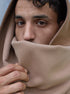 Portrait rapproché d’un homme portant une écharpe beige en polyester recyclé, portée en capuche et cache-cou, avec finition douce et fermeture invisible par aimants